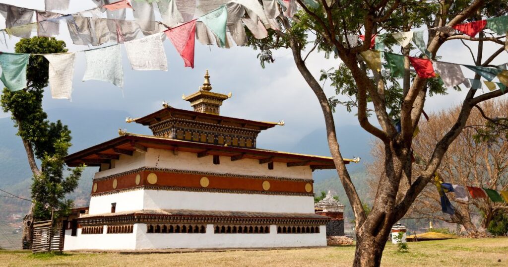 這張圖片展示了不丹切米拉康寺廟,寺廟外掛滿了象徵祝福的經幡,背景是寧靜的山景。
