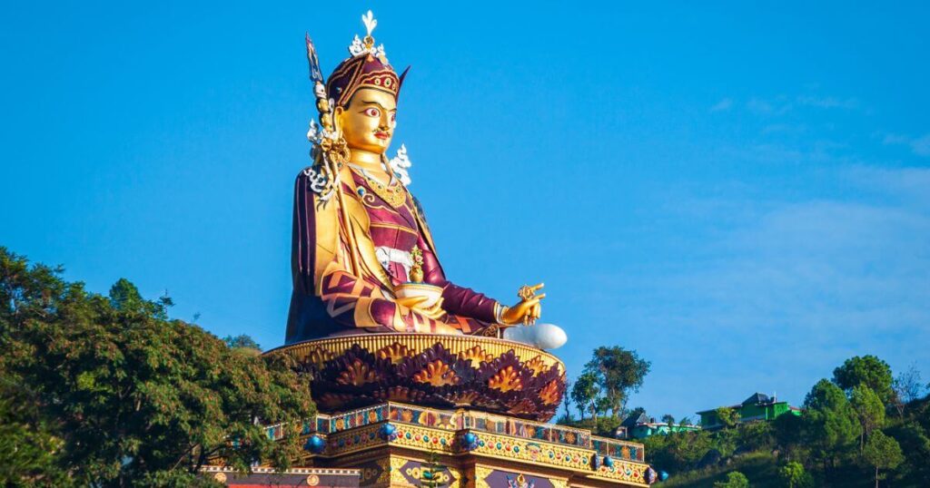 該圖片展示了位於印度喜馬偕爾邦(Himachal Pradesh)的蓮花生大士(Guru Rinpoche)巨型雕像。藍天下的金色雕像坐落在山巔,象徵著當地深厚的佛教文化與信仰。雕像的精緻細節與周圍的自然景色相融合,為朝聖者提供了一個寧靜且充滿靈性的場所。