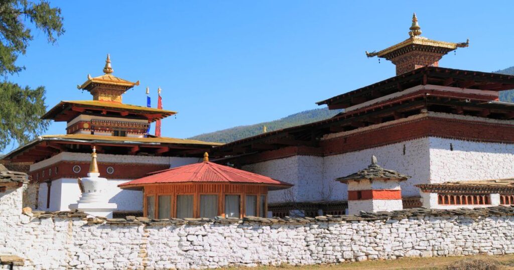 這張圖片展示了不丹帕羅的朱雀寺,該寺廟是當地最古老的佛教寺廟之一,擁有獨特的不丹建築風格,白色石牆搭配紅色屋頂,並裝飾著傳統的佛教符號。此寺廟是佛教徒朝聖的重要地點,承載著悠久的歷史與文化遺產。