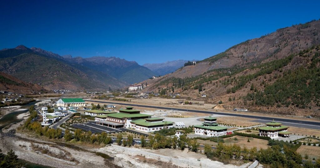 這張圖片展示了不丹帕羅國際機場的全景，機場被高山環繞，遠處是藍天白雲，顯示出這個世界上最具挑戰性的降落地之一。