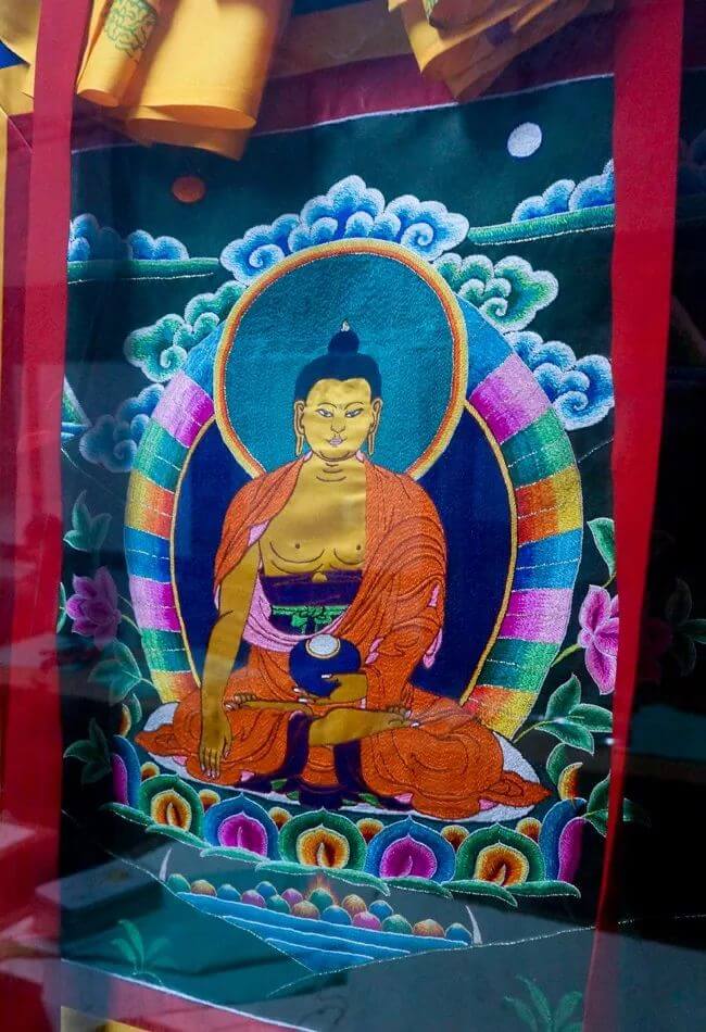 該圖片展示了一幅精美的佛教刺繡作品,中央為一位佛祖的形象,四周以鮮豔的顏色和花紋裝飾,傳達了不丹宗教藝術的虔誠與美麗。